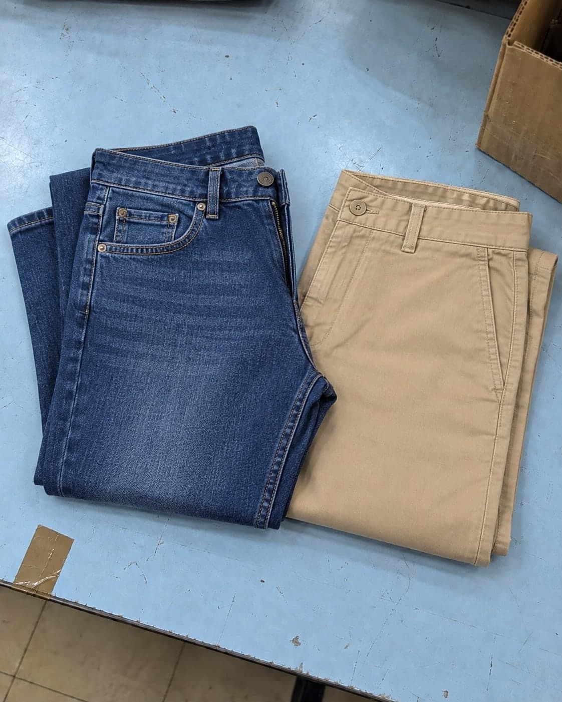 Indigo jeans and sand-coloured trousers folded on a stock counter