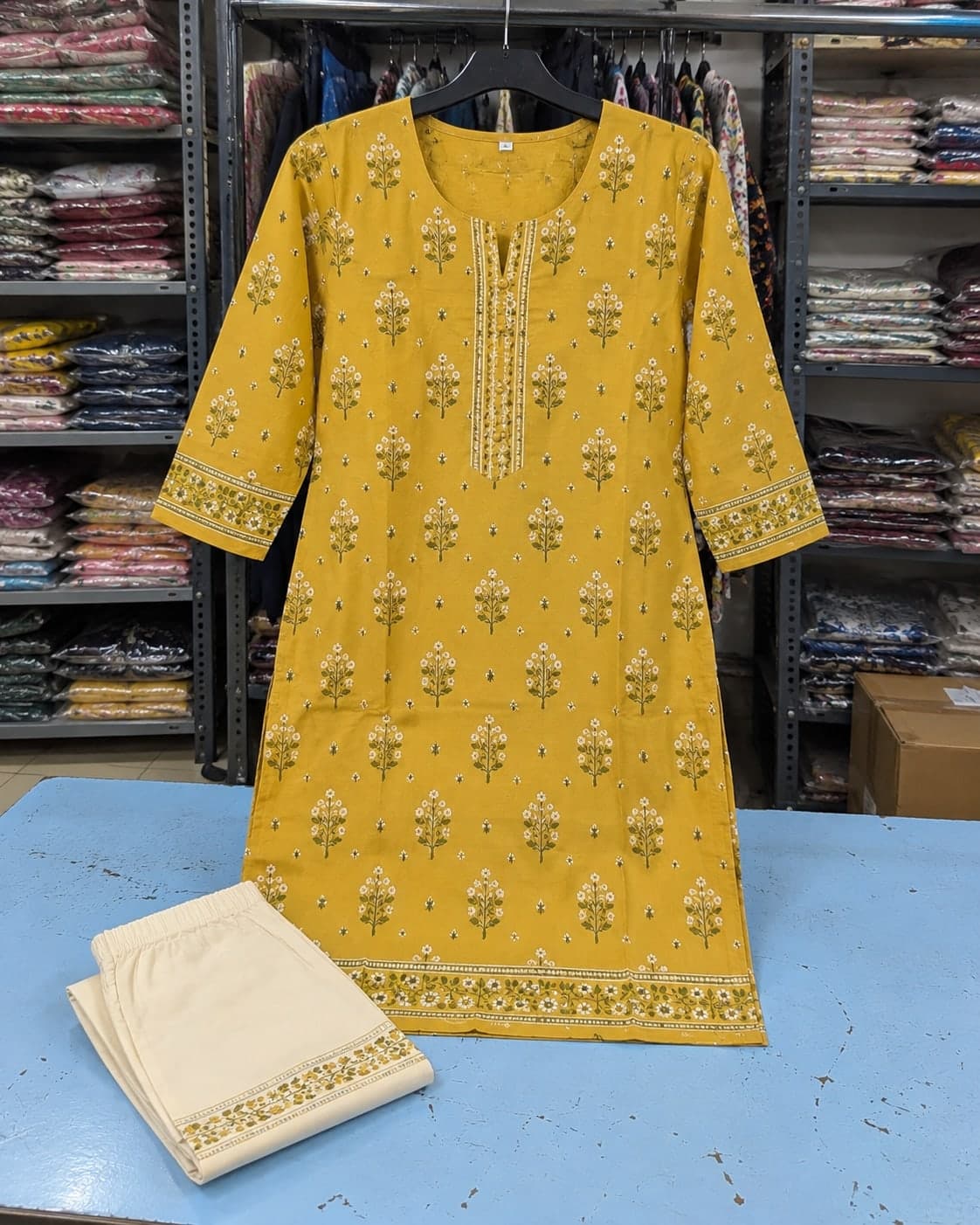 A mustard printed kurta on a shop hanger with matching cream trousers