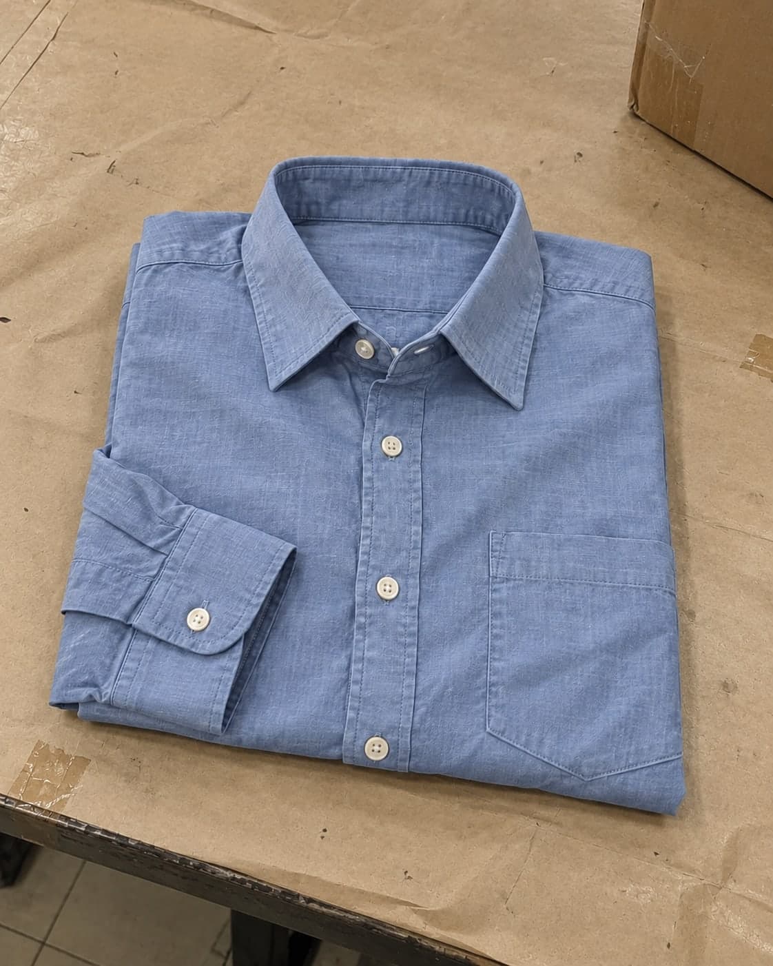 A pale blue cotton shirt folded loosely on a packing table