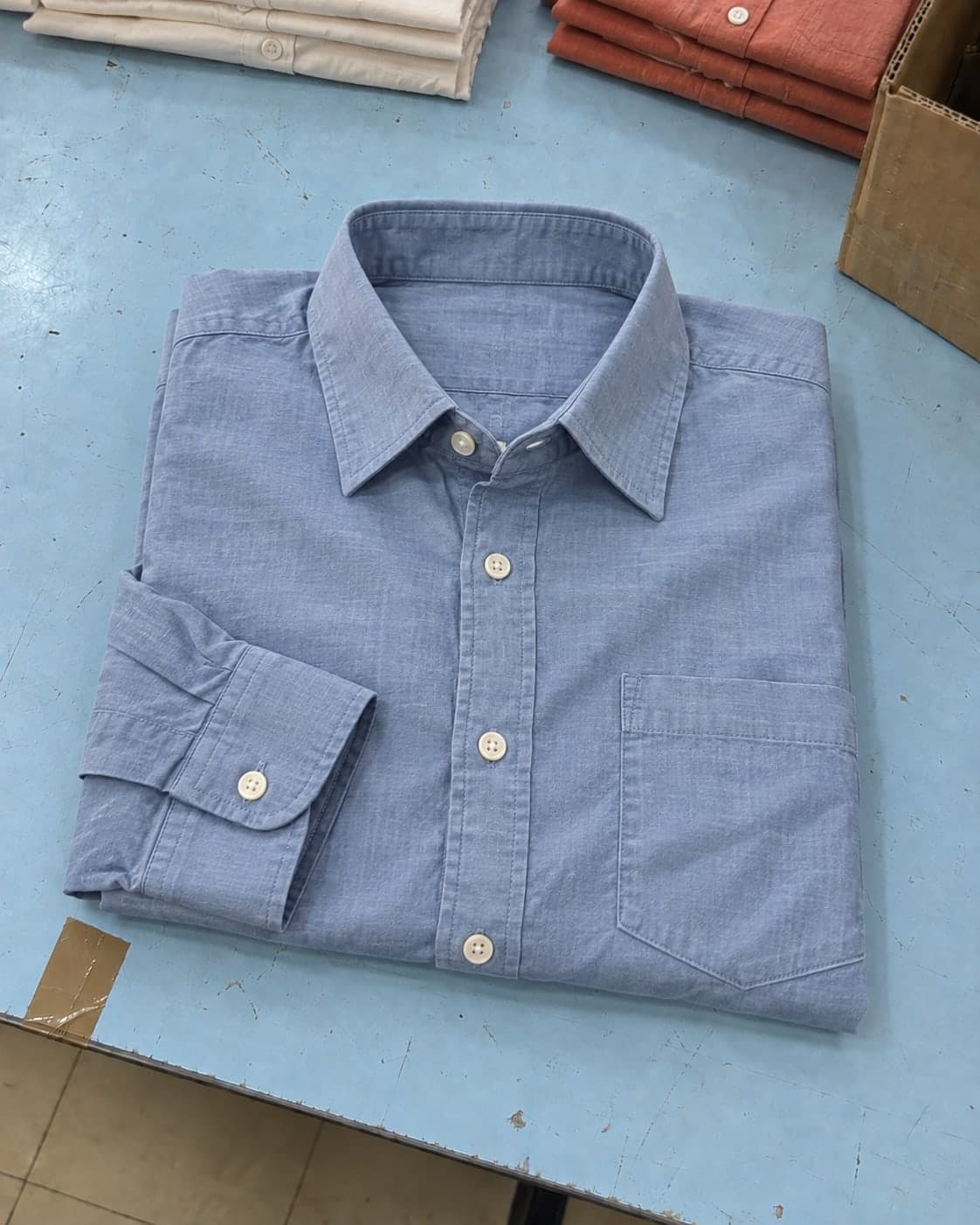 A pale blue cotton shirt folded loosely on a packing table