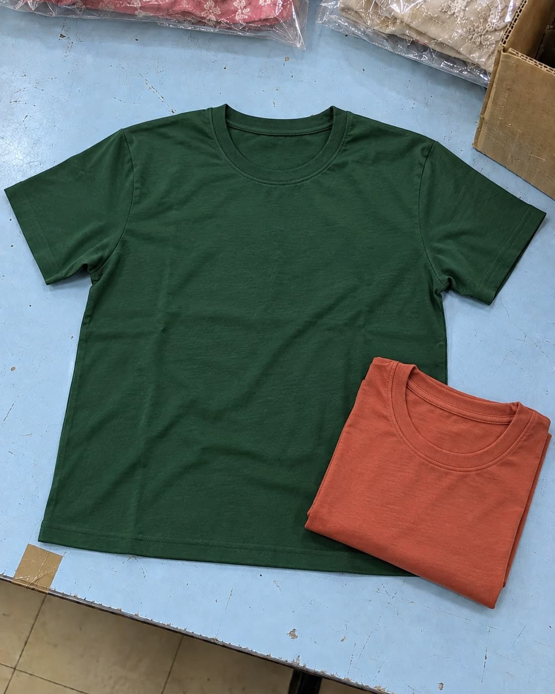 A green cotton T-shirt laid open beside a folded terracotta T-shirt