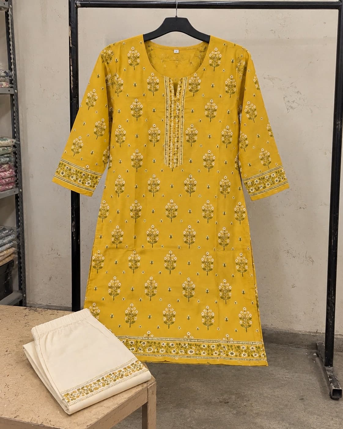 A mustard printed kurta on a shop hanger with matching cream trousers